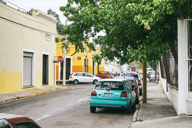 Merida / Yucatan, Mexico - June 1, 2015: The green cars parking on the stree of city of Merida with the colorful yellow building in background, Yucatan, Mexico