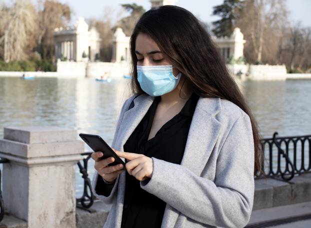 Woman,With,Face,Mask,Using,Her,Mobile,In,The,Retiro