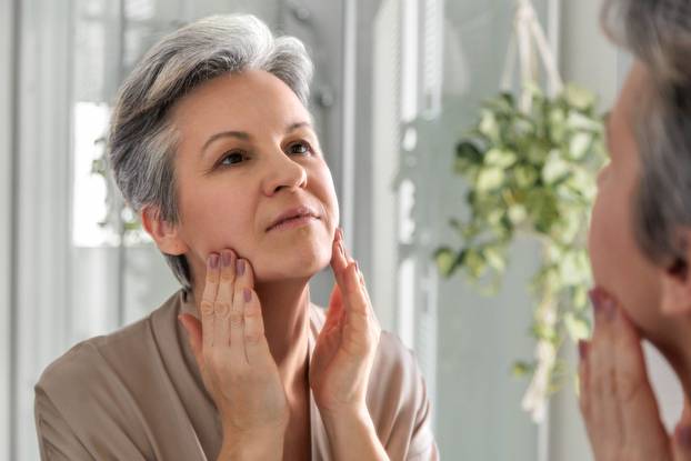 Smiling elderly woman of the age of a pensioner iwith gray hair does herself a manual facial massage