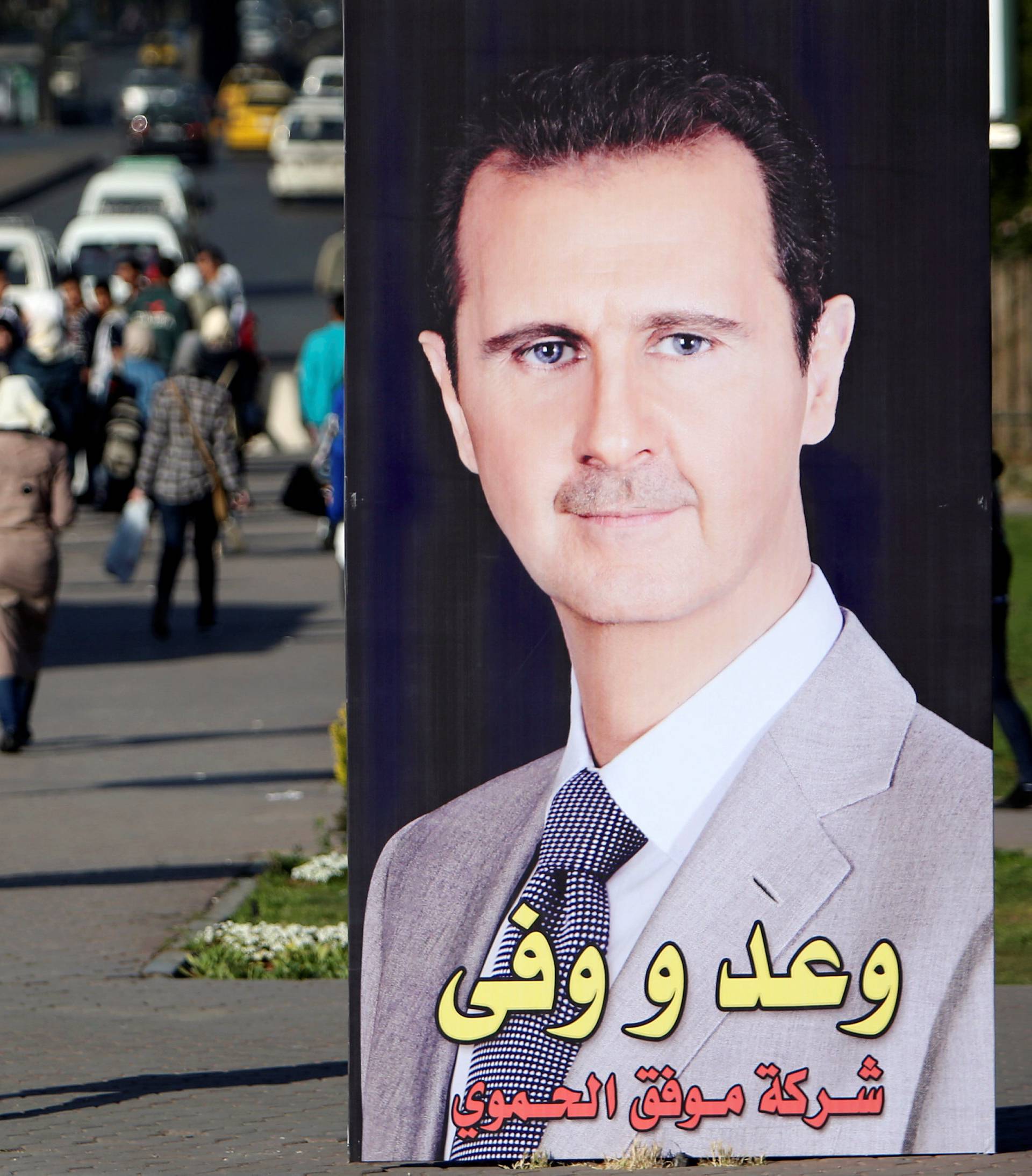 A woman walks near a picture of Syrian President Bashar al Assad in Damascus