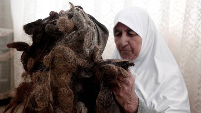 Ezzeya Daraghmeh, an 82-year-old Palestinian woman who said she has kept parts of her hair she cut over 67 years, holds her collected hair as she stuffs it in a pillow, in the West Bank town of Tubas