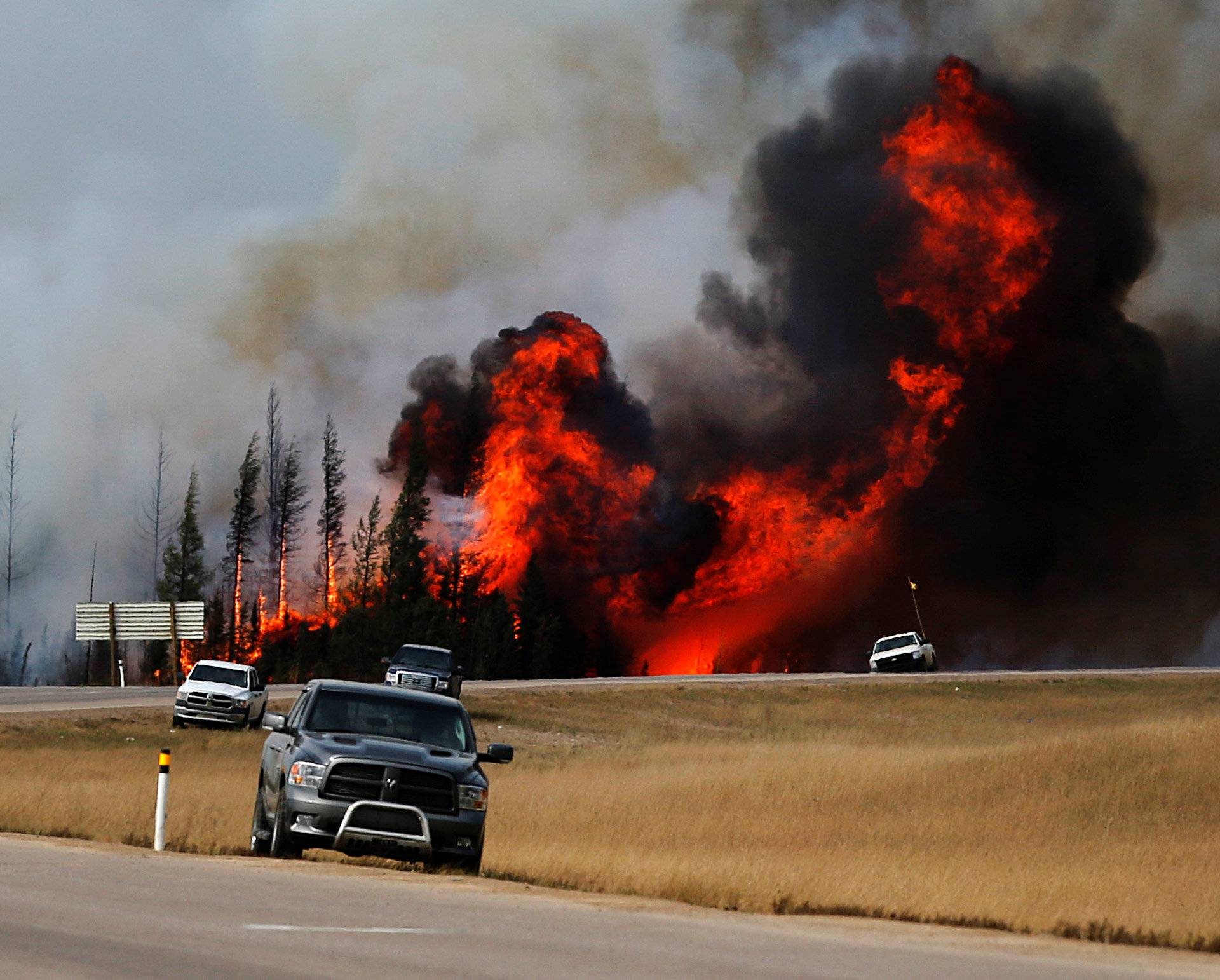 Smoke and flames from the wildfires erupt behind cars on the highway near Fort McMurray