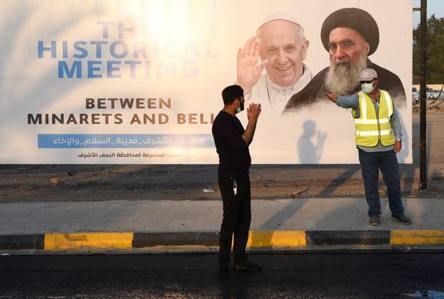 Workers gesture near a poster of Pope Francis and Iraq