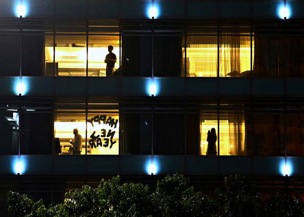 People stand at a hotel with a sign "Happy New Year" in one of its windows, during New Year