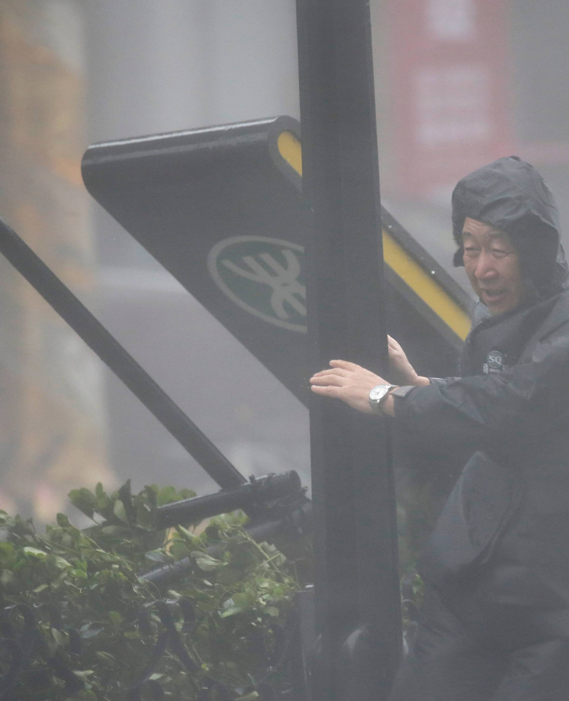 A security personnel holds onto a pole next to a subway sign in the rainstorm as Typhoon Mangkhut approaches, in Shenzhen