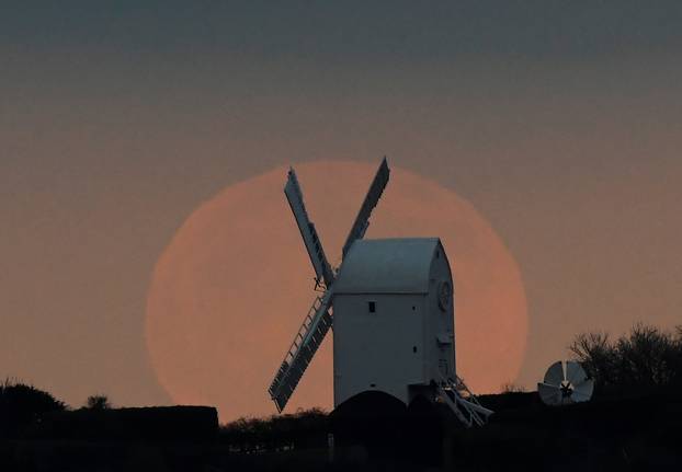 The full moon is seen rising behind a windmill on the Sussex Downs near Brighton, Britain