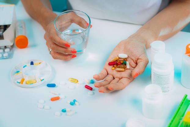 Supplementation. Woman holding a myriad of vitamin and mineral supplements in her hand.