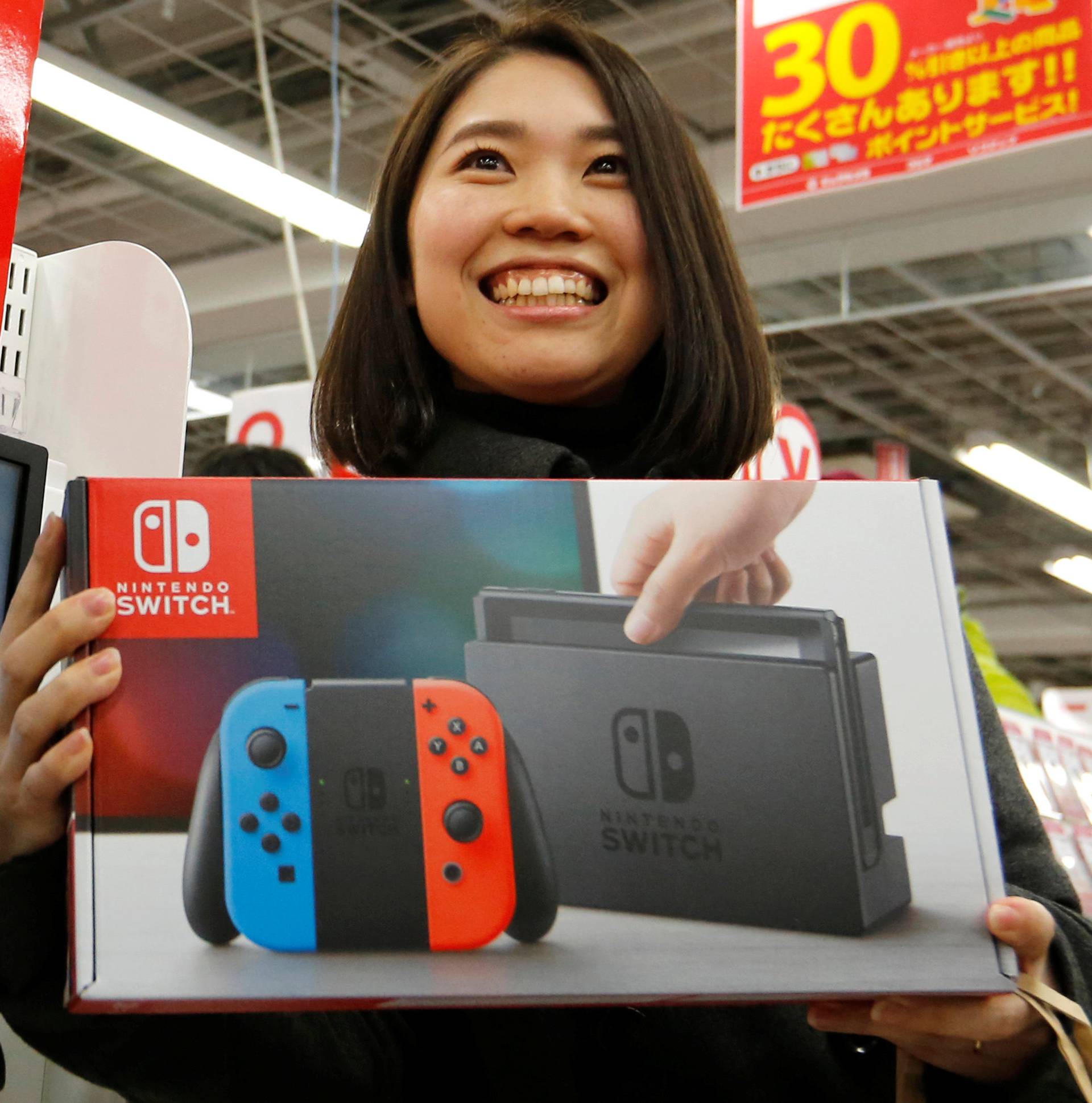 Nao Imoto smiles as she poses with her Nintendo Switch game console after buying it at an electronics store in Tokyo