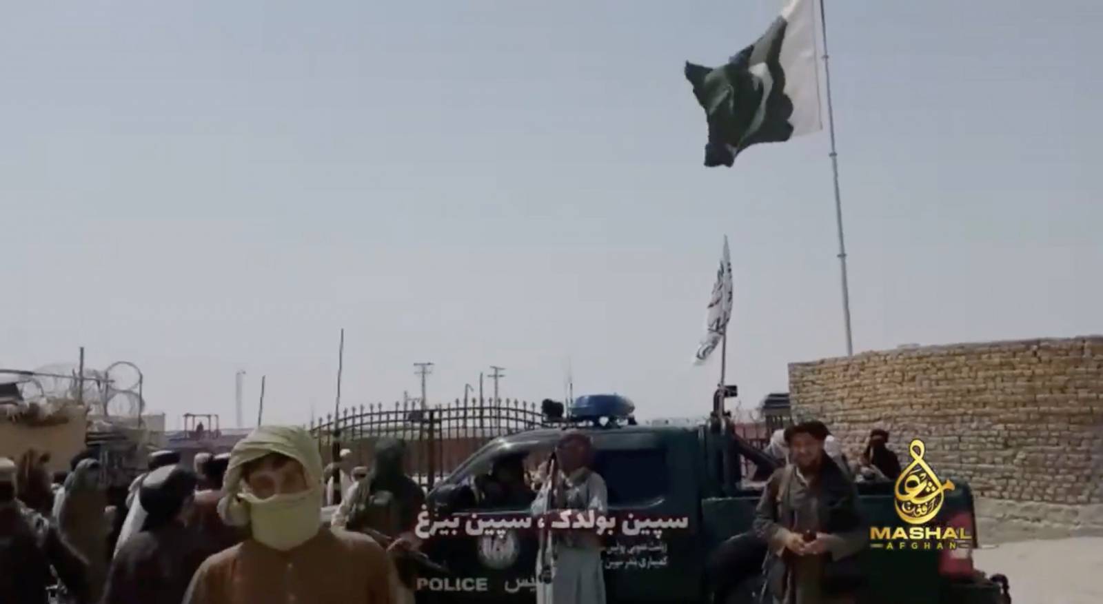 People stand in front of a vehicle as an Islamic Emirate of Afghanistan and a Pakistan's flag flutter in front of the friendship gate of Afghanistan and Pakistan at the Wesh-Chaman border crossing