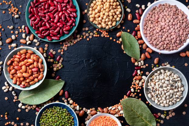 Legumes, overhead shot on a black background with a place for text. Lentils, soybeans, chickpeas, red kidney beans, a vatiety of pulses with bay leaves, forming a frame