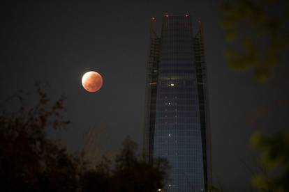 A partial lunar eclipse dubbed the 'blood moon' is seen next to the Gran Torre building in Santiago
