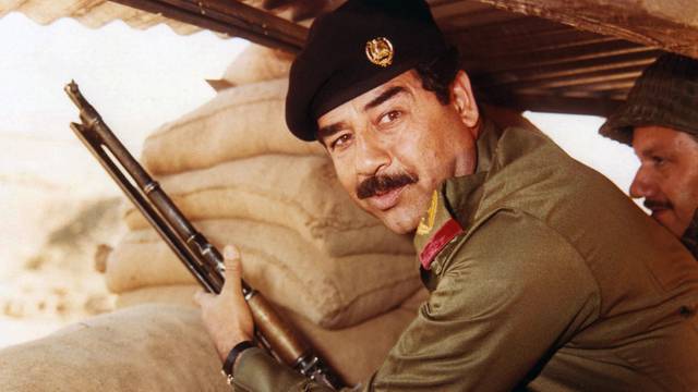 Iraq: Saddam Hussein, President of Iraq 1979-2003, posing with a rifle in a dugout during the Iran-Iraq War (1980-1988) <br/><br/>