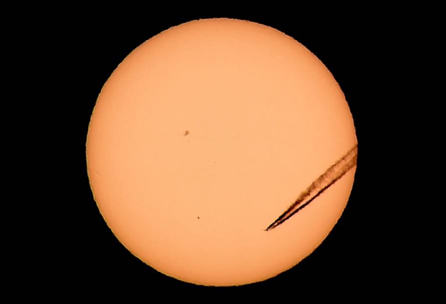 A jet airliner leaves a vapor trail as the planet Mercury is seen, lower left quadrant, transiting across the face of the sun in Las Vegas