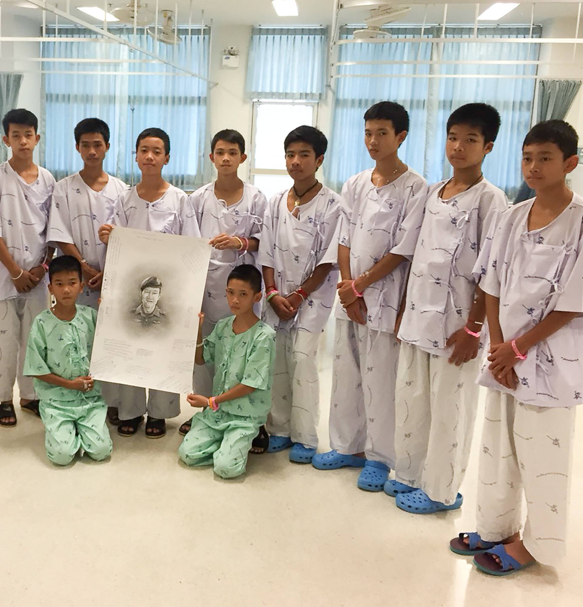 The 12-member "Wild Boars" soccer team and their coach rescued from a flooded cave pose with a drawing picture of Samarn Kunan, a former Thai navy diver who died working to rescue them at the Chiang Rai Prachanukroh Hospital, in Chiang Rai