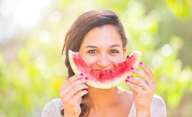 Beautiful young woman at park eating a slice of watermelon