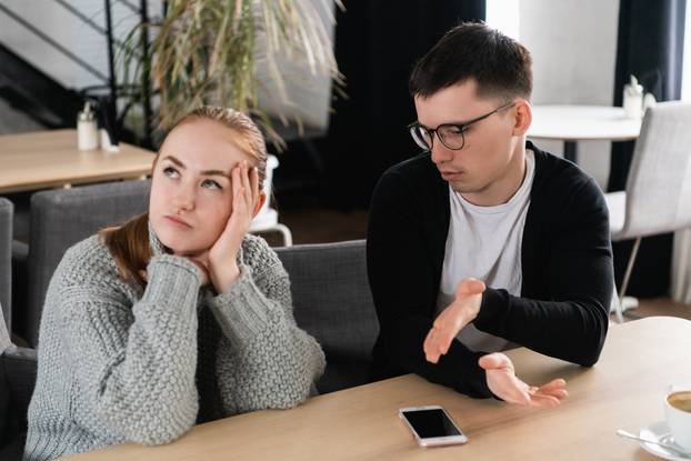 Annoyed man trying to explain something to his wife sitting on a couch in the cafe