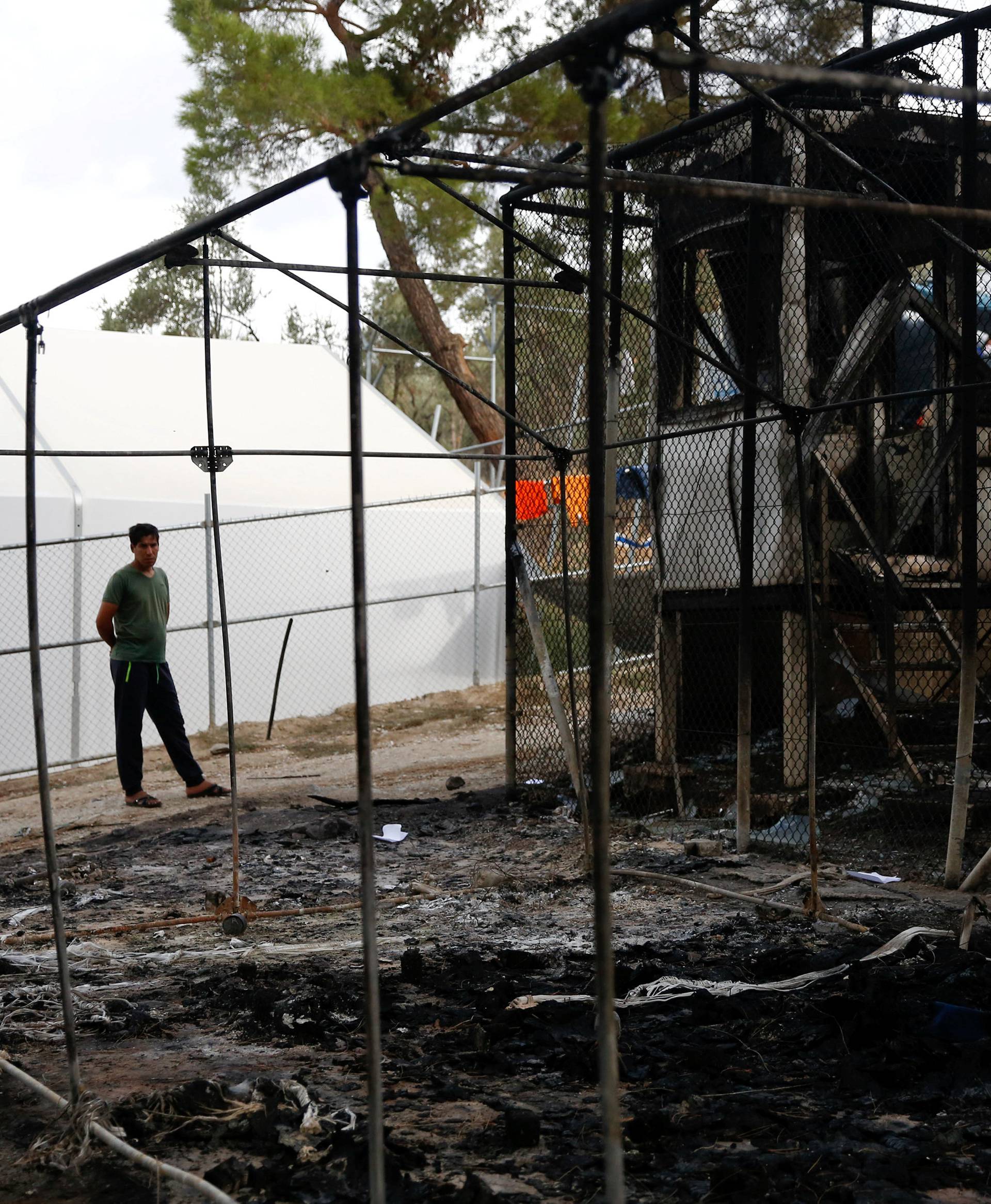 A migrant stands next to a burned tent at the Moria migrant camp, after a fire at the facility, on the island of Lesbos