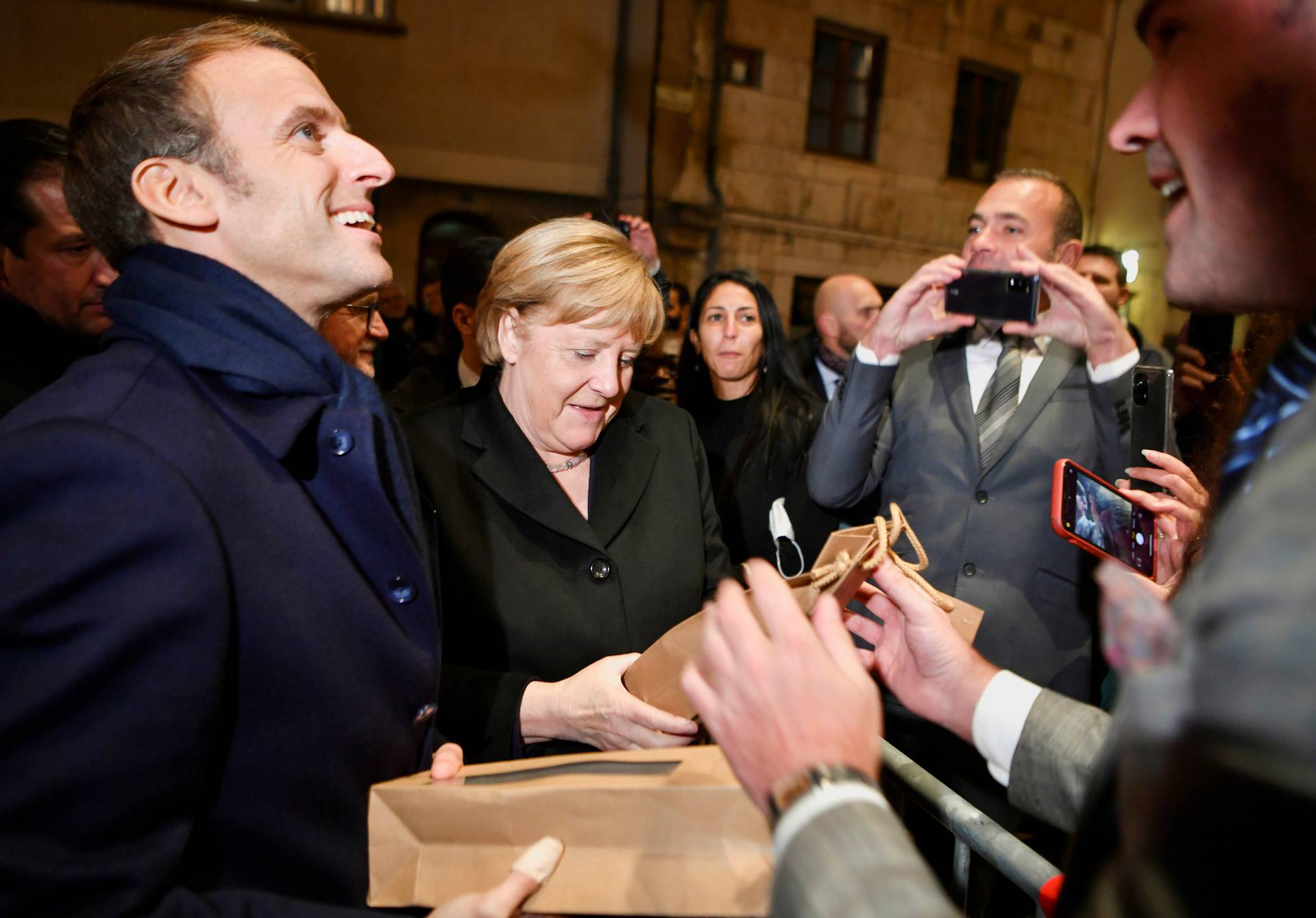 Outgoing German Chancellor Angela Merkel and France's President Emmanuel Macron receive flowers and a bottle of wine as gifts upon their arrival for talks, in Beaune