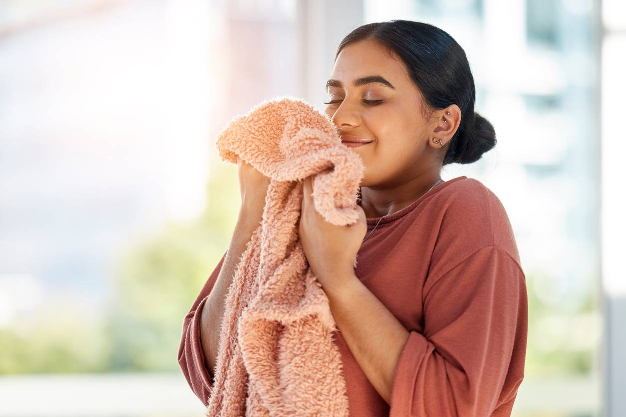 Woman smelling clean laundry, blanket or fabric for fresh and clean smell in house after doing washing, cleaning and housekeeping. Happy female cleaner with textile for aroma, fragrance and scent