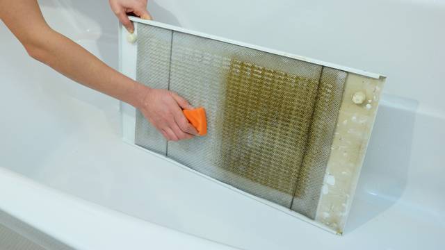 Woman cleaning kitchen hood filter in bath tub with sponge