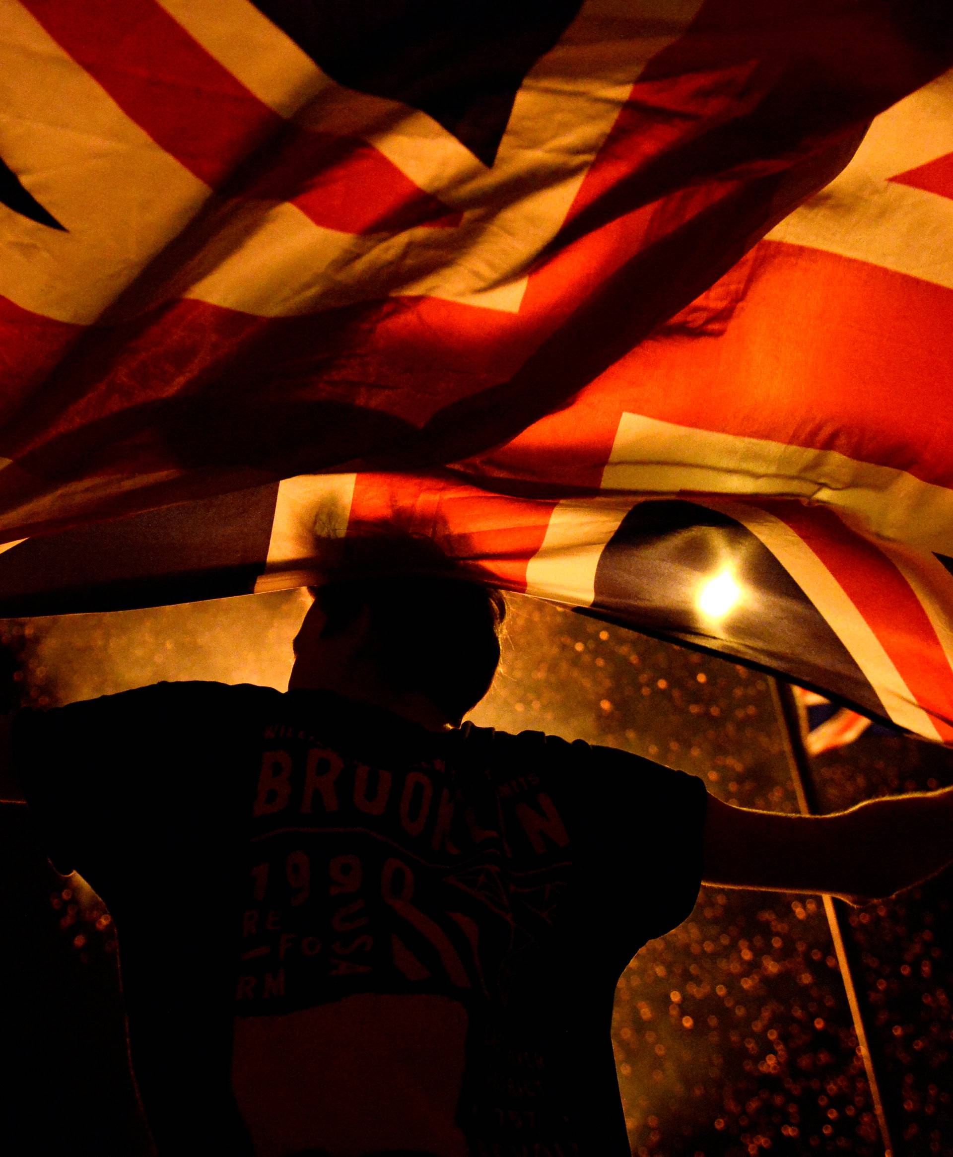 A boy holds a Union Jack flag in front of a bonfire burning in the Shankill Road area ahead of the Twelfth of July celebrations held by members of the Orange Order in Belfast