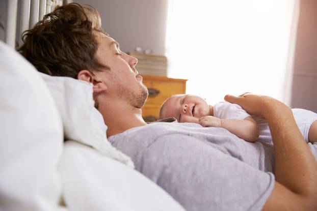 Father Sleeping In Bed Holding Newborn Baby Daughter