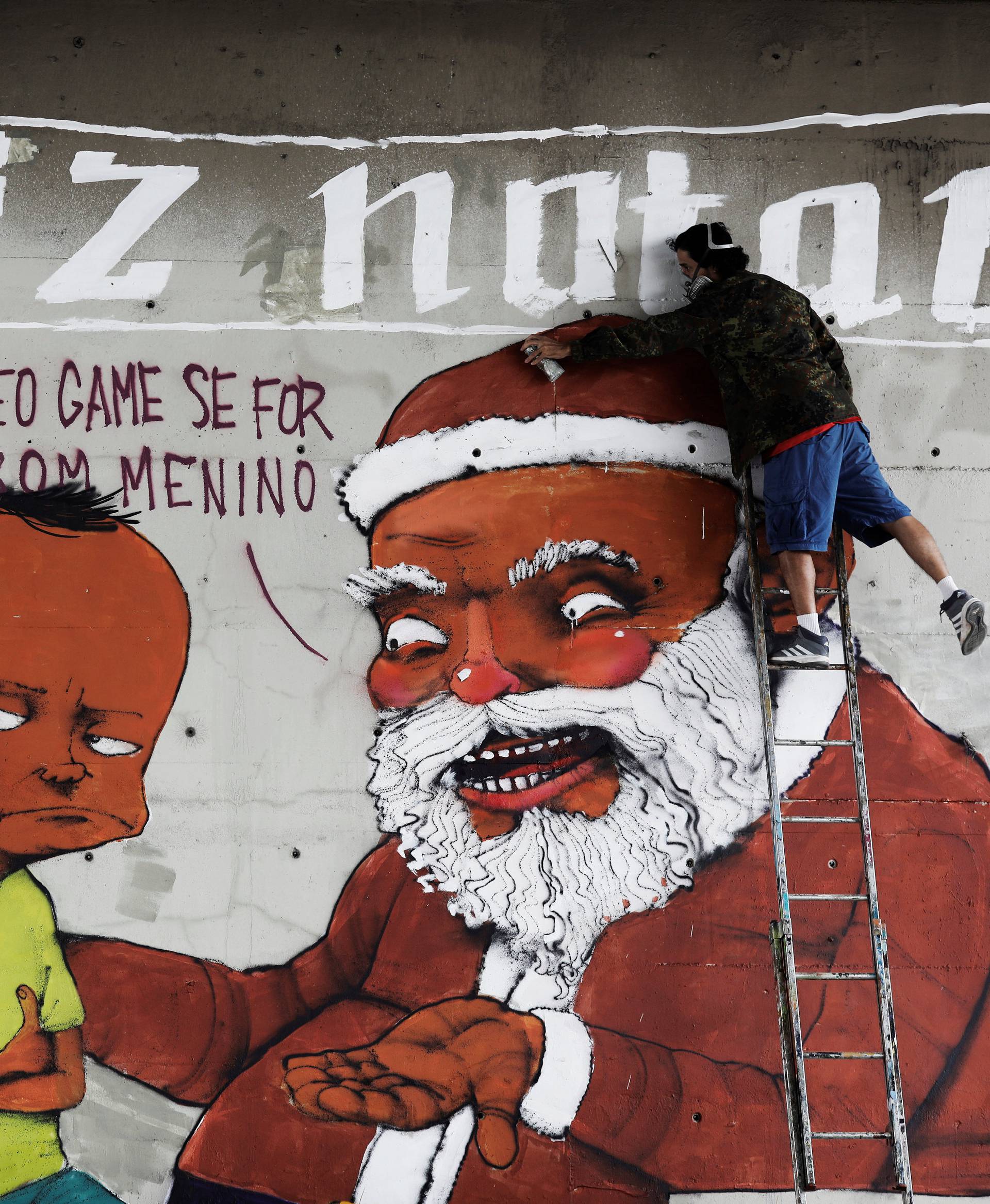 Brazilian artist Paulo Ito puts the final touches to his Christmas graffiti, depicting Santa Claus and a boy, on a wall underneath