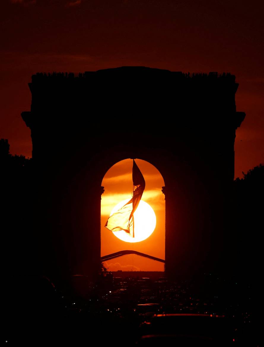 The sun is seen in the middle of the Arc de Triomphe on the Champs Elysees