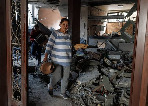 A woman collects belongings from the rubble of her house, which she says was damaged by an Israeli strike