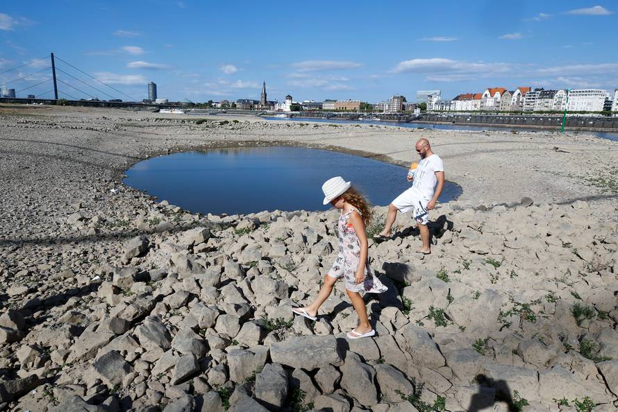 A family walks next to a puddle in the partially dried riverbed of Rhine, in front of the skyline of Dusseldorf