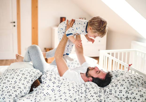 Father with a toddler boy having fun in bedroom at home at bedtime.