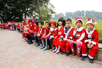 Children wearing Santa Claus outfits sit along Hoan Kiem Lake in Hanoi, Vietnam