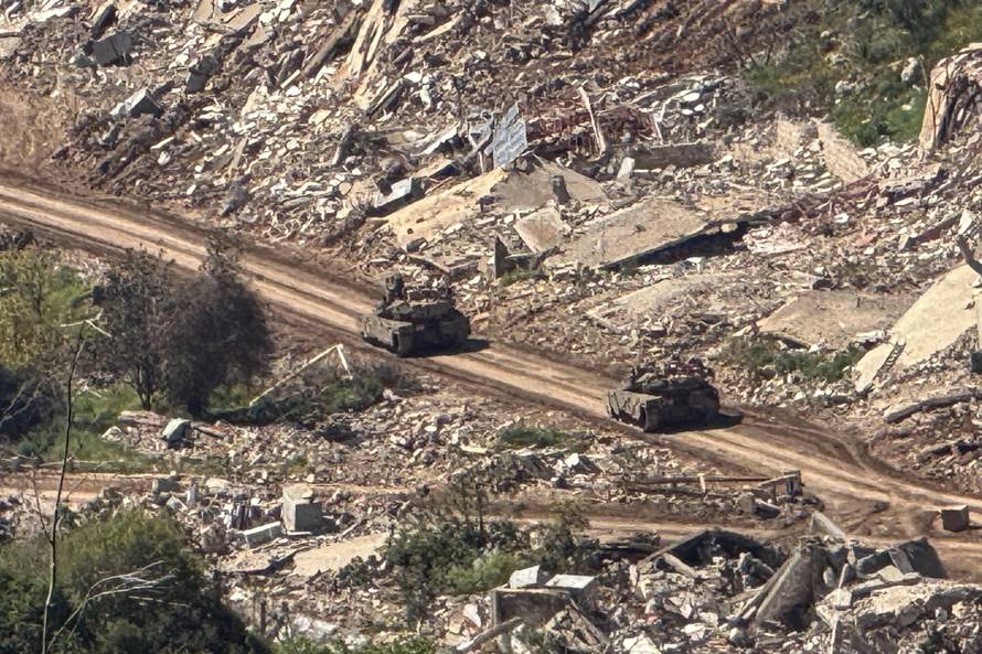 Israeli tanks drive on a road on the Lebanese side of the Israel-Lebanon border, as seen from northern Israel