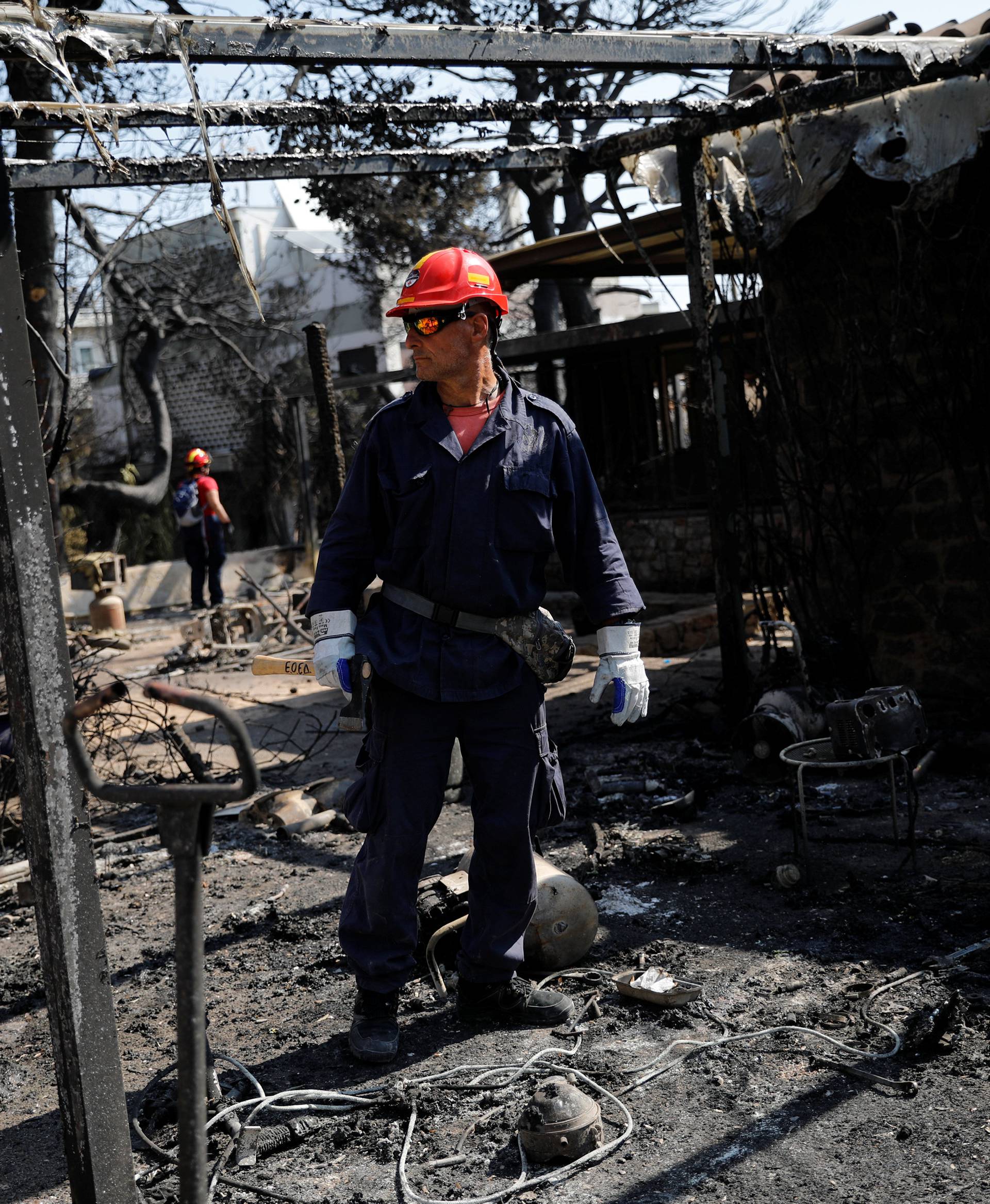 A member of a rescue team searches inside a destroyed building following a wildfire at the village of Mati