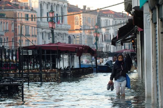 A woman wades through a flooded street during high tide in Venice