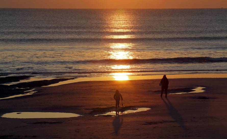 People watch the sun as it sets over the Atlantic Ocean on a cold day in Les Sables d'Olonne 