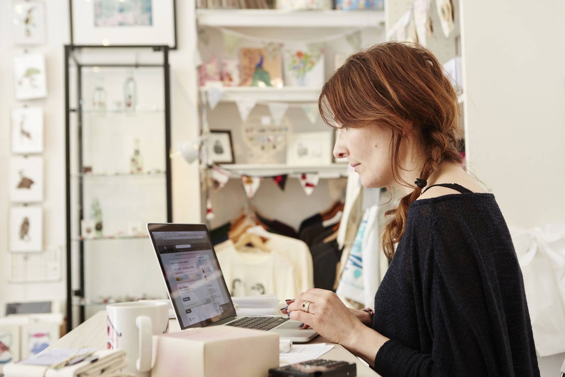 A woman in a small crafts supplier and gift shop, using a laptop, working,