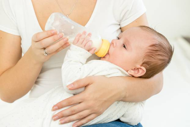 Mother giving milk from bottle to her baby sleeping on hands