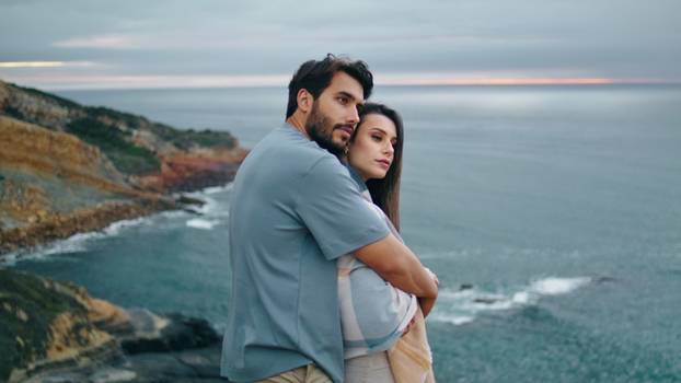 Peaceful couple standing coast hill looking gloomy seascape. Man hugging woman