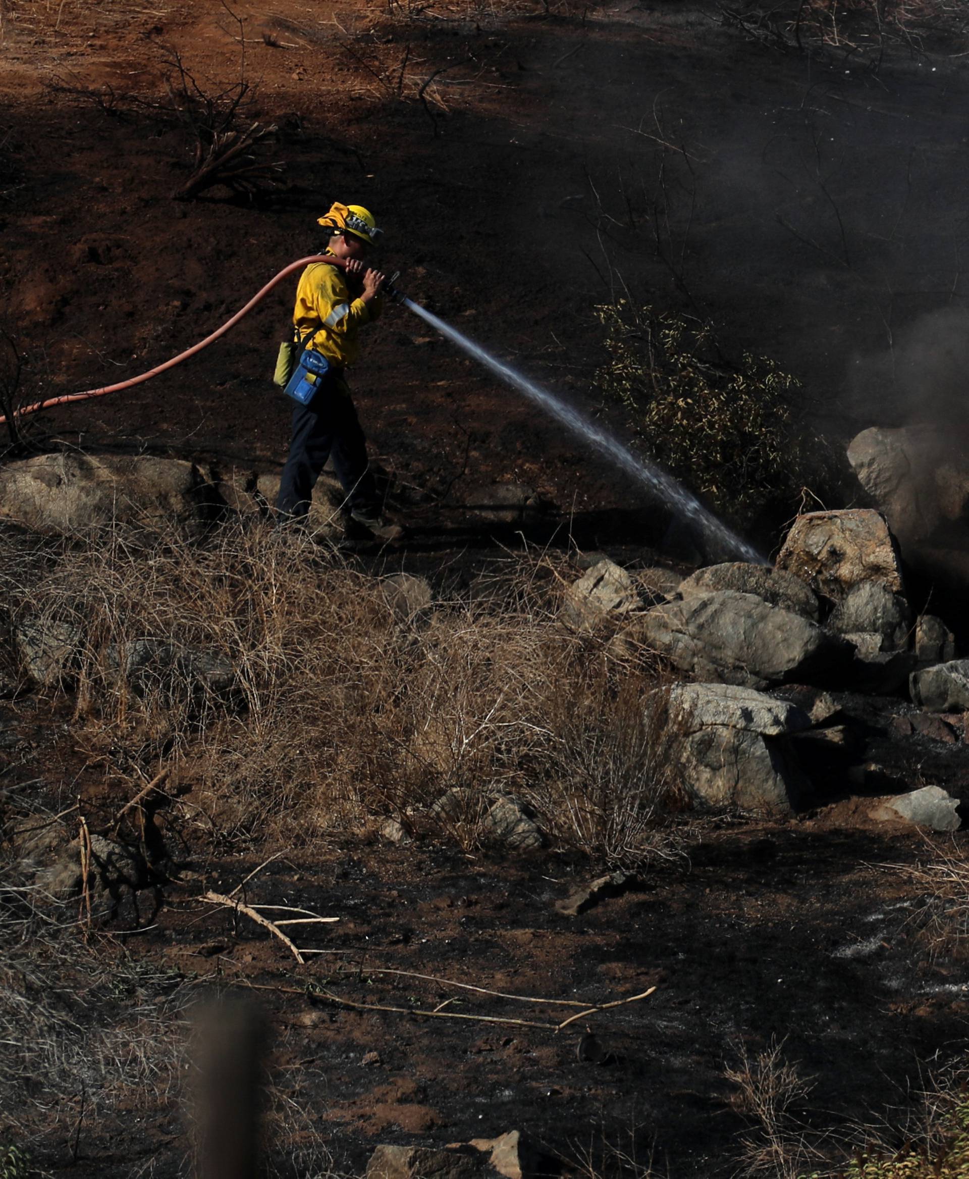 A firefighter puts water on a hotspot caused by the Lilac Fire, a fast moving wildfire in Bonsall, California
