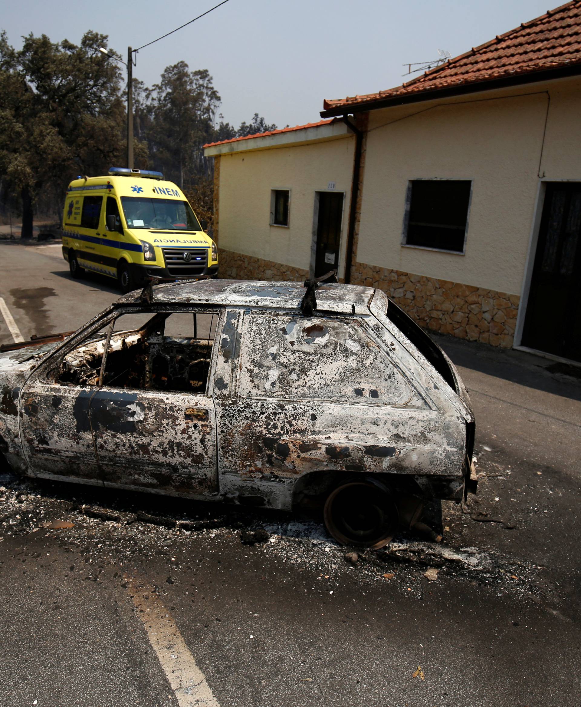 An ambulance drives past a burned car during a forest fire in Figueiro dos Vinhos