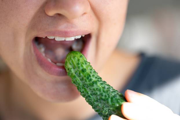 Detailed shot of a woman eats fresh cucumber.