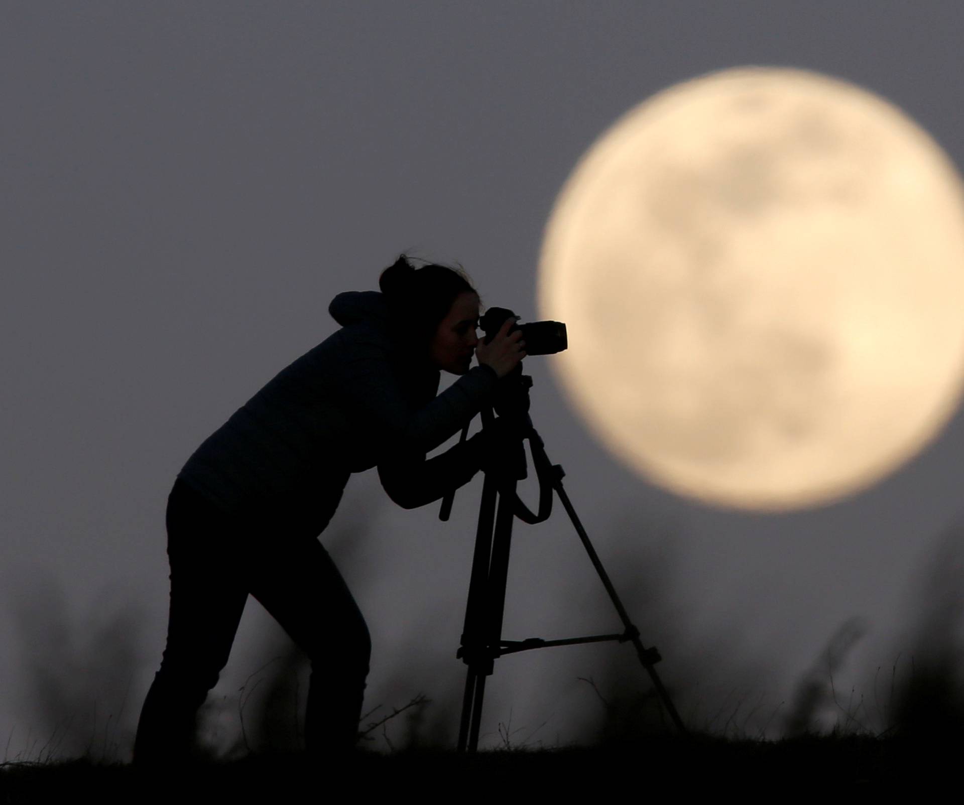A woman photographs the Pink Supermoon over mountain Smetovi, during an astronomical event that occurs when the moon is closest to the Earth in its orbit, making it appear much larger and brighter than usual, in Zenica