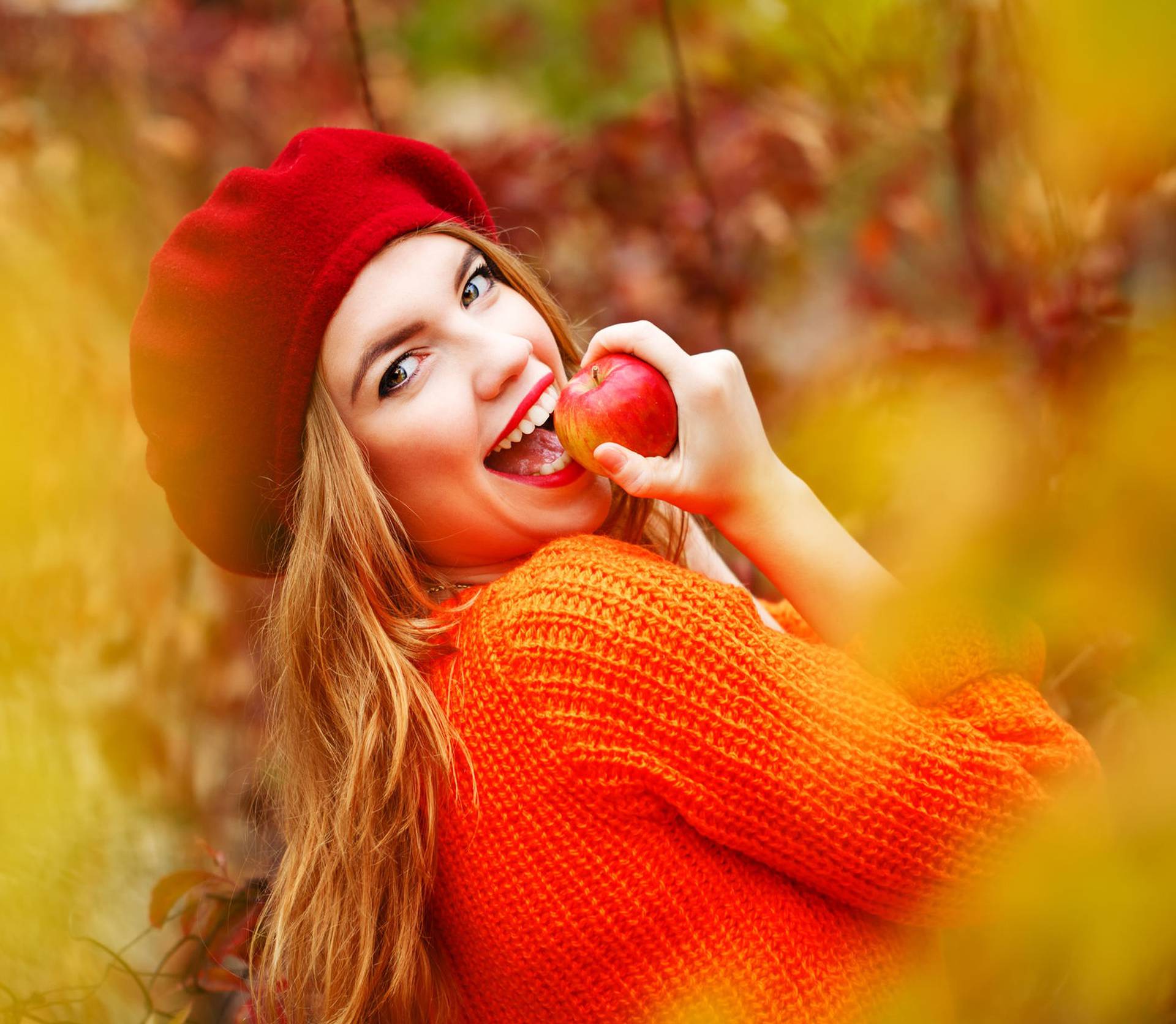Lovely girl in beret and sweater, holding ripe apple and smiling