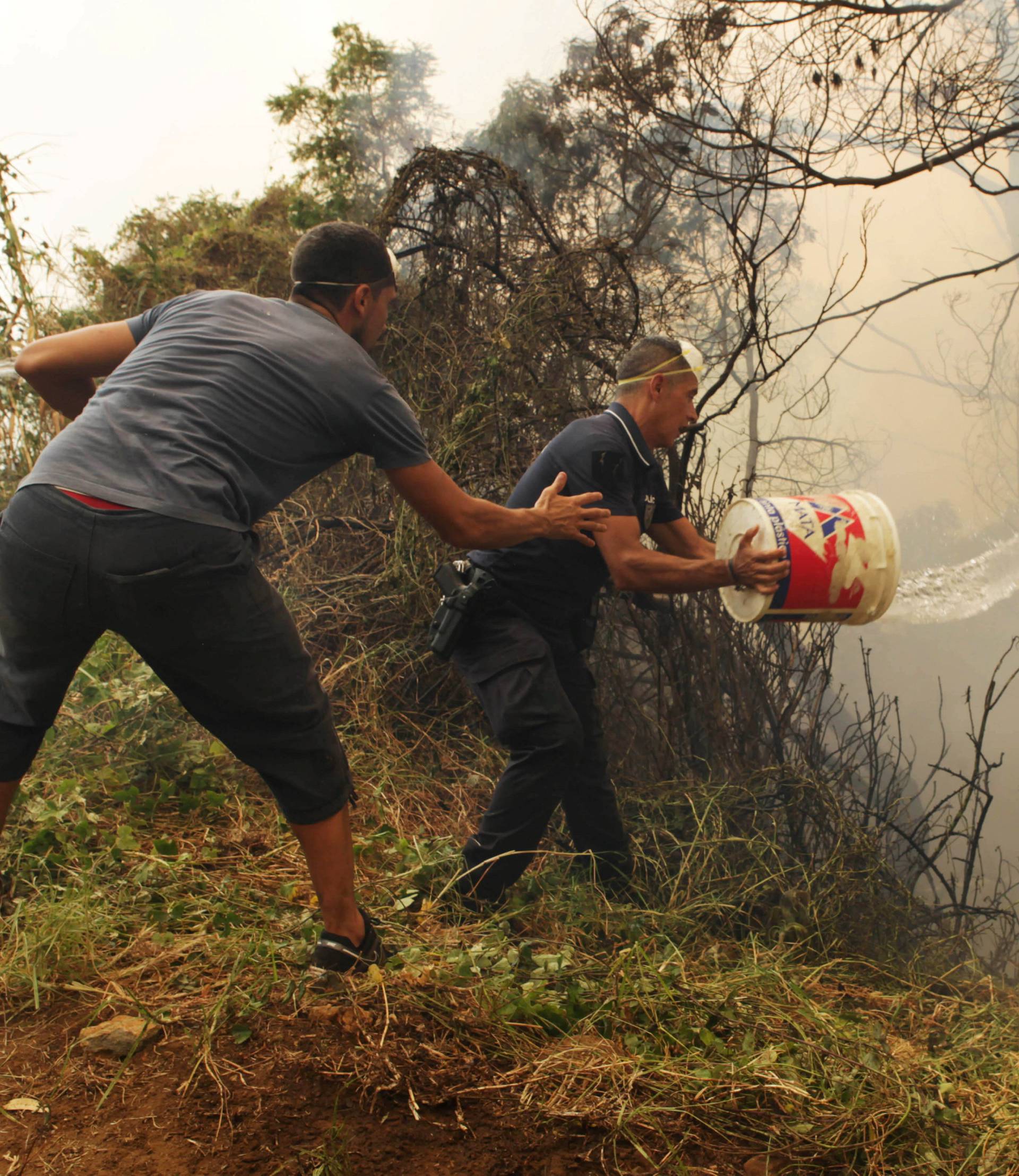 Civilians, and police officers use water buckets to help extinguish a forest fire near houses at Sao Joao Latrao, Funchal, Madeira island