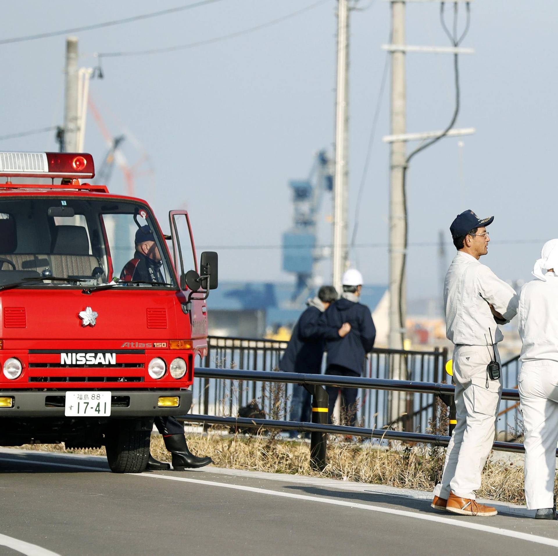 Firefighters and local residents look toward the port to check the water level after tsunami advisories were issued following an earthquake in Soma