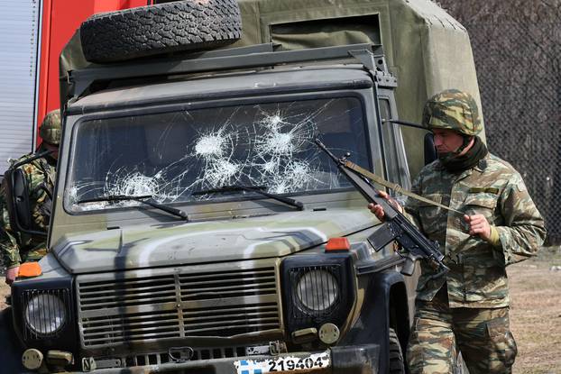 A Greek soldier stands next to an army vehicle with broken windshield as migrants who want to cross into Greece from Turkey