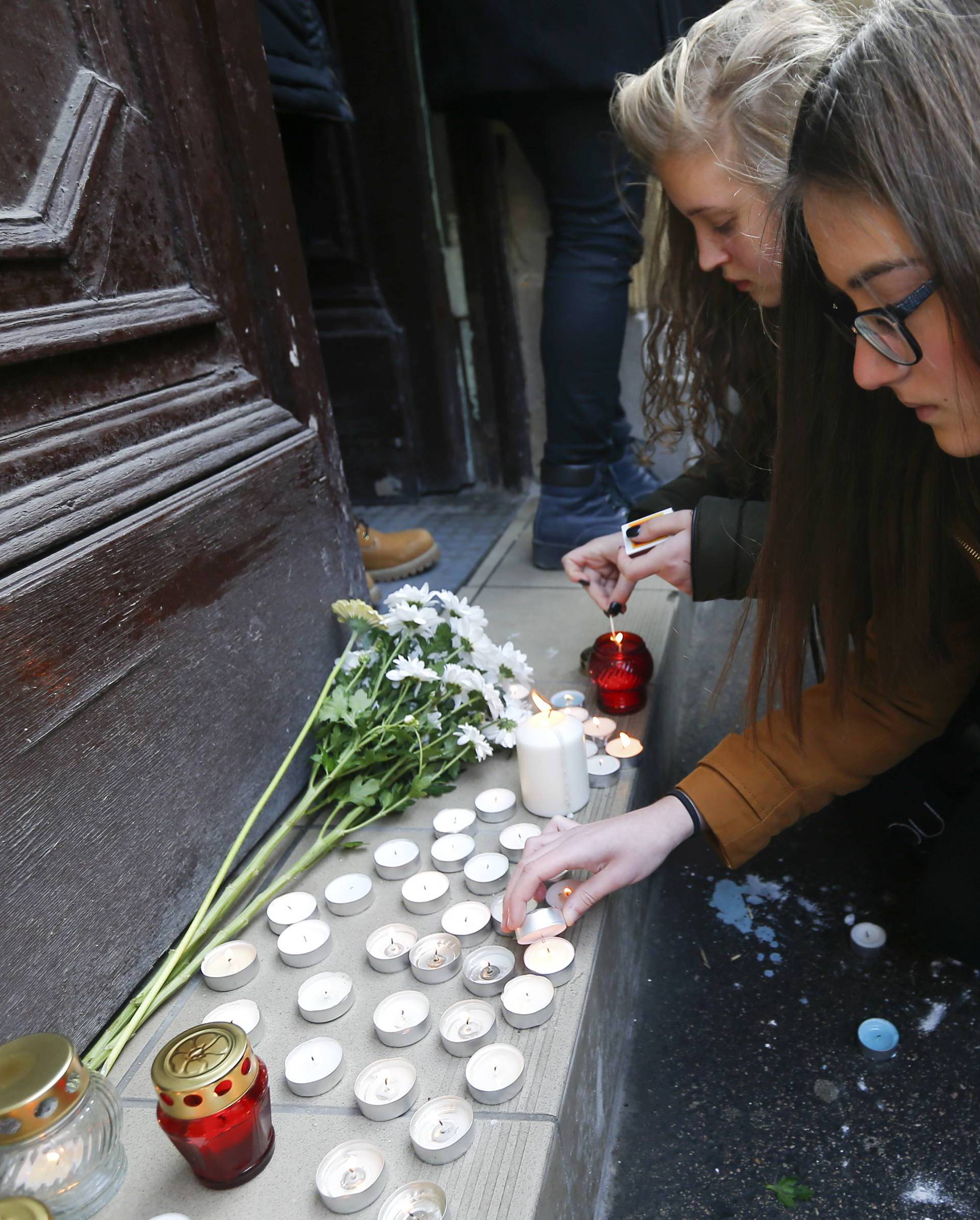 People light candles in front of a school building in Budapest