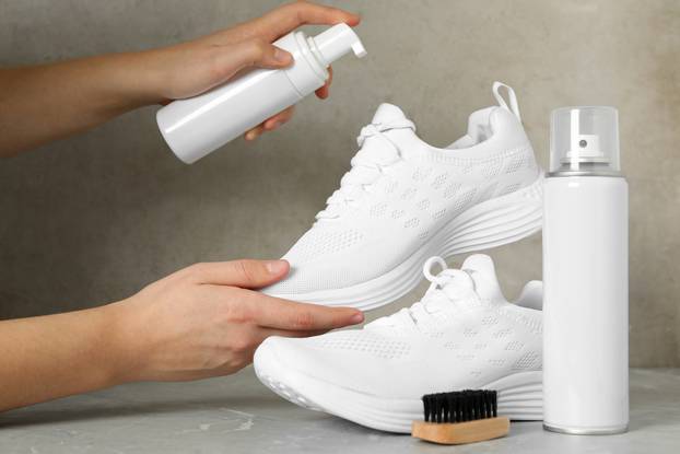 Woman cleaning stylish footwear on grey marble background, close