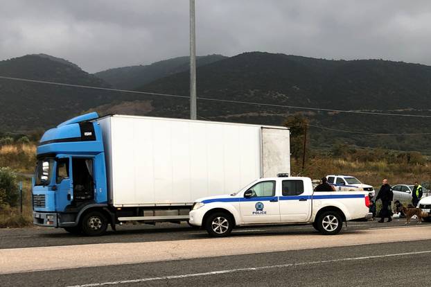 Police officers stand next to a refrigerated truck carrying migrants, after a check at a motorway near Xanthi